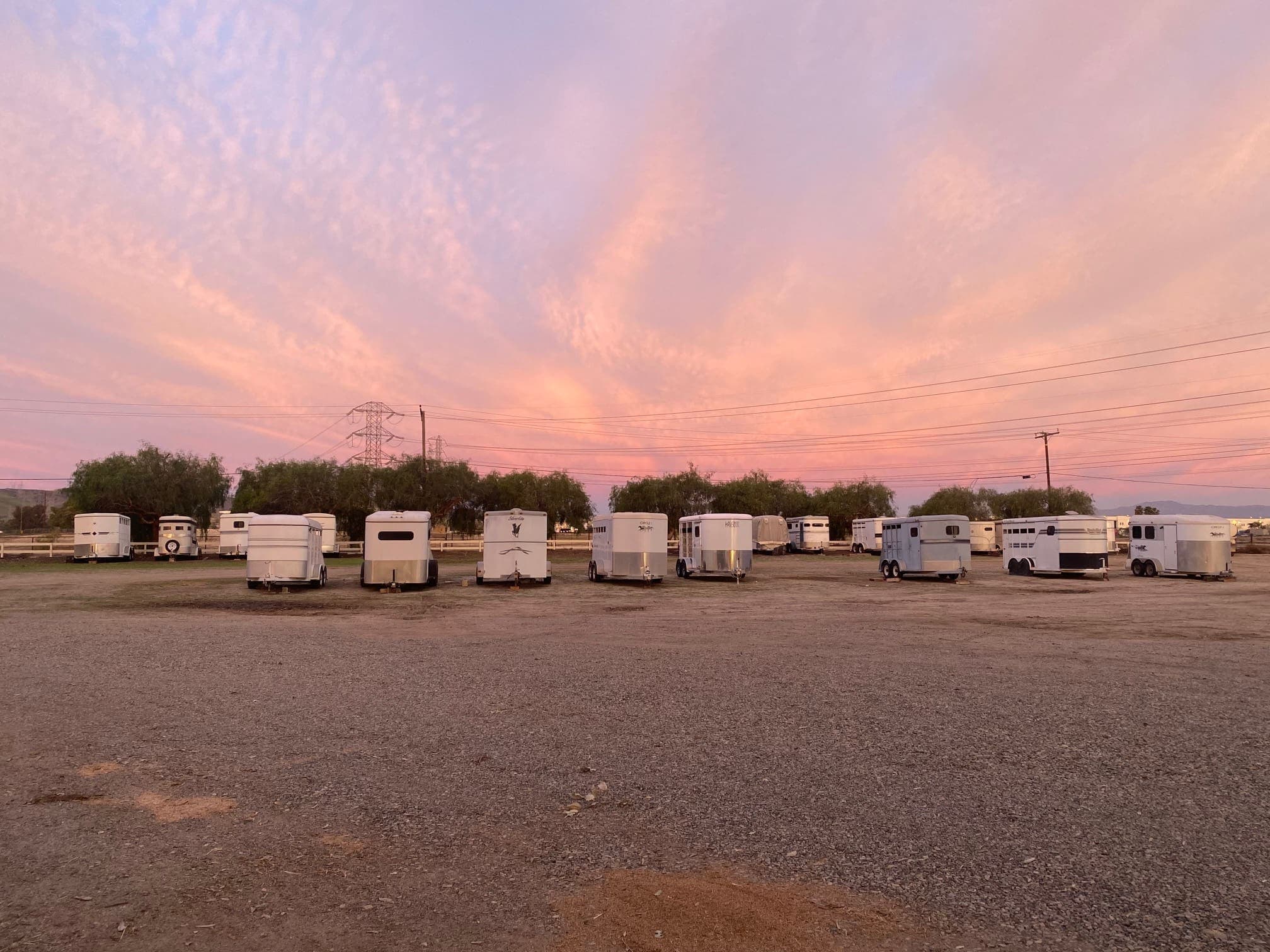 A row of horse trailers parked on the dry lot under a pink and lavender dusk sky